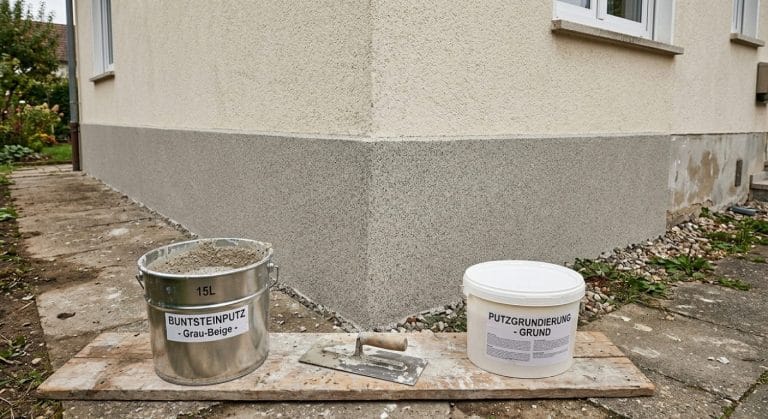 Sockel mit Buntsteinputz in gesprenkelter grau-beiger Optik, davor Eimer und Edelstahlkelle